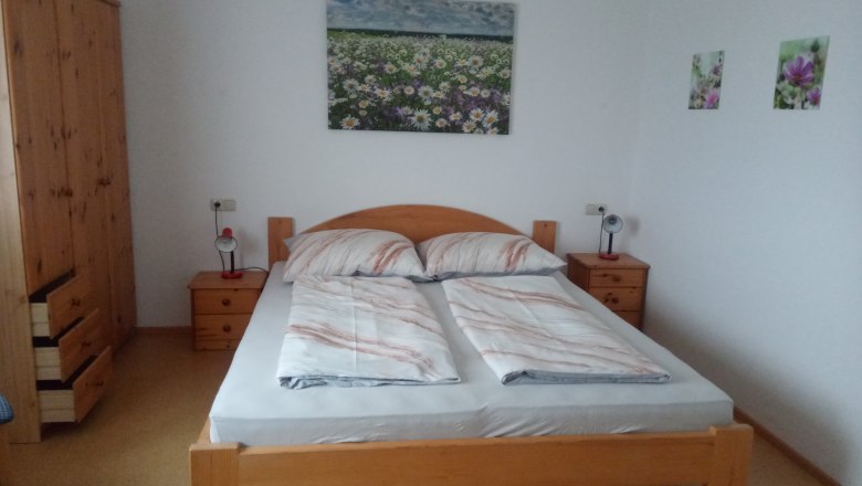 Bedroom with double bed, wooden furniture and flower pictures on the wall.