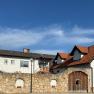 A building with red tiled roofs and a stone wall in the foreground under a blue sky.