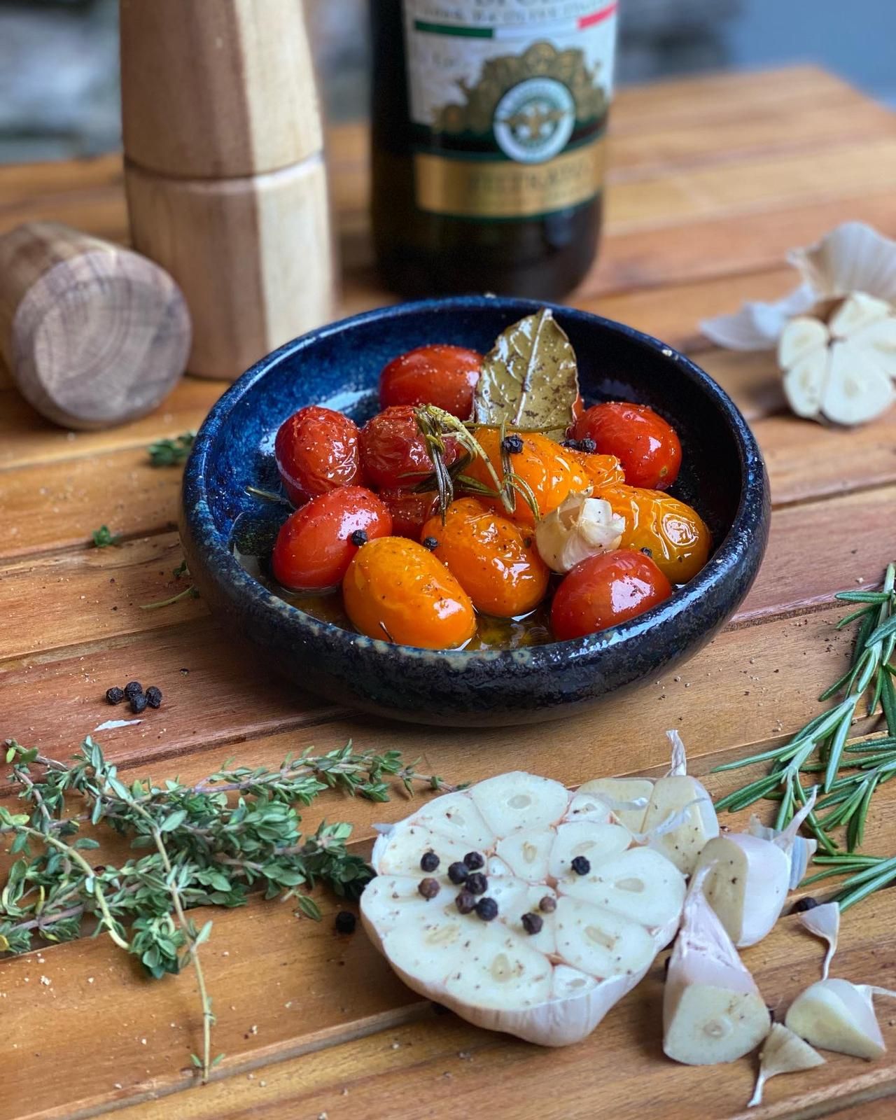 A bowl of confit tomatoes, garlic and herbs on a wooden table.