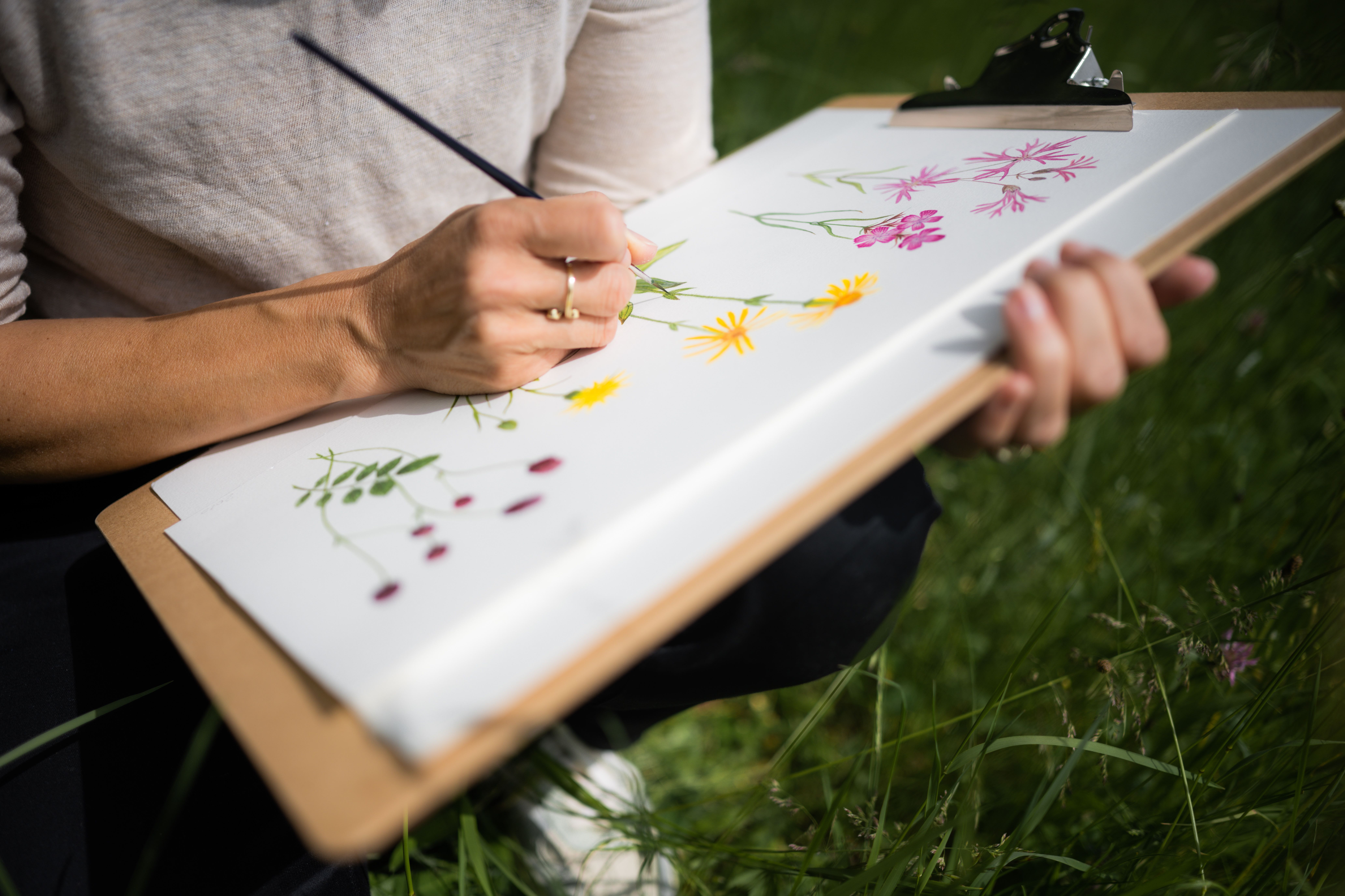 A person paints flowers on a clipboard outdoors.