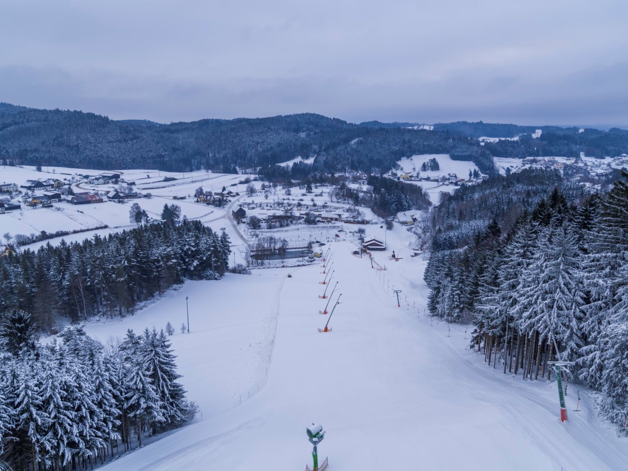 Snow-covered ski slope in Kirchbach, surrounded by forests and hills.