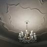 A chandelier hangs from a decorative ceiling with stucco decorations.