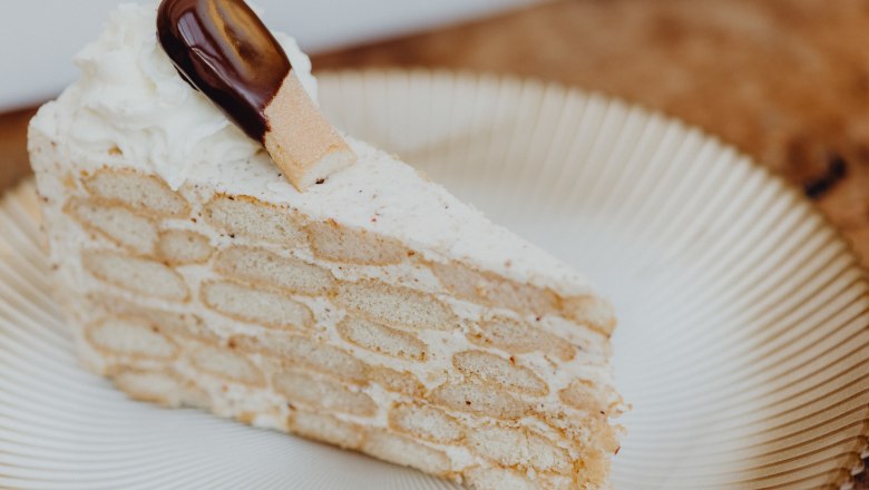 A slice of Malakoff cake on a plate, decorated with cream and a chocolate cookie.