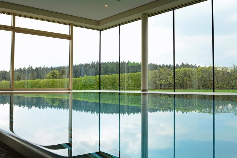 Indoor pool with large windows and views of the forest and hedges.
