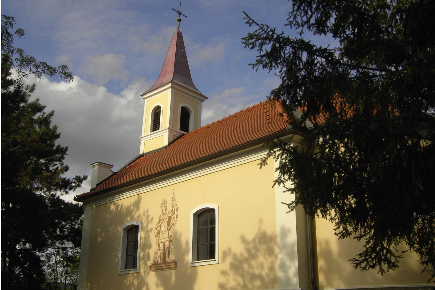 Floriani Chapel Oberrohrbach with tower and mural, surrounded by trees.
