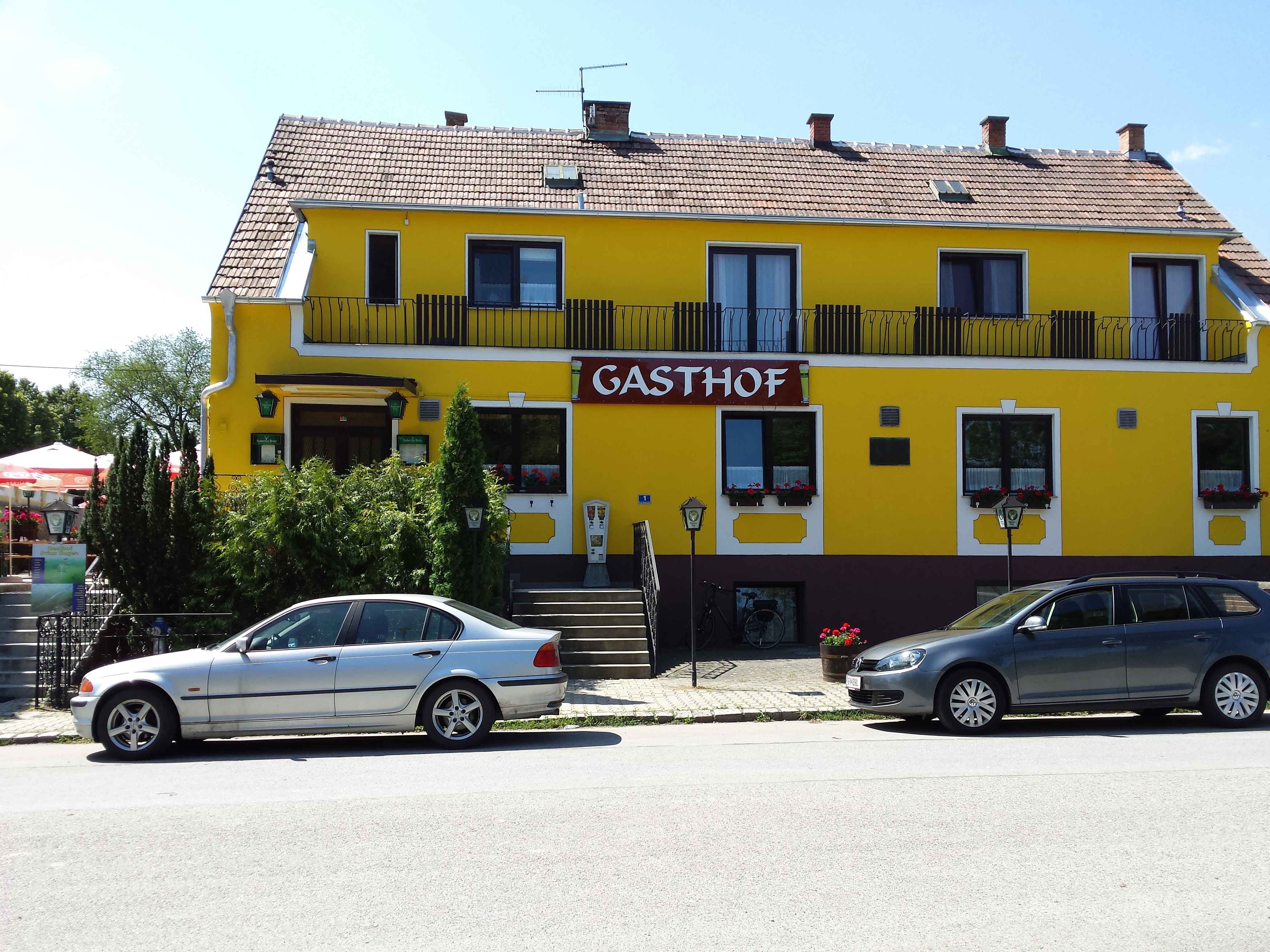 Yellow building with the inscription 'Gasthof', two parked cars in front of it.