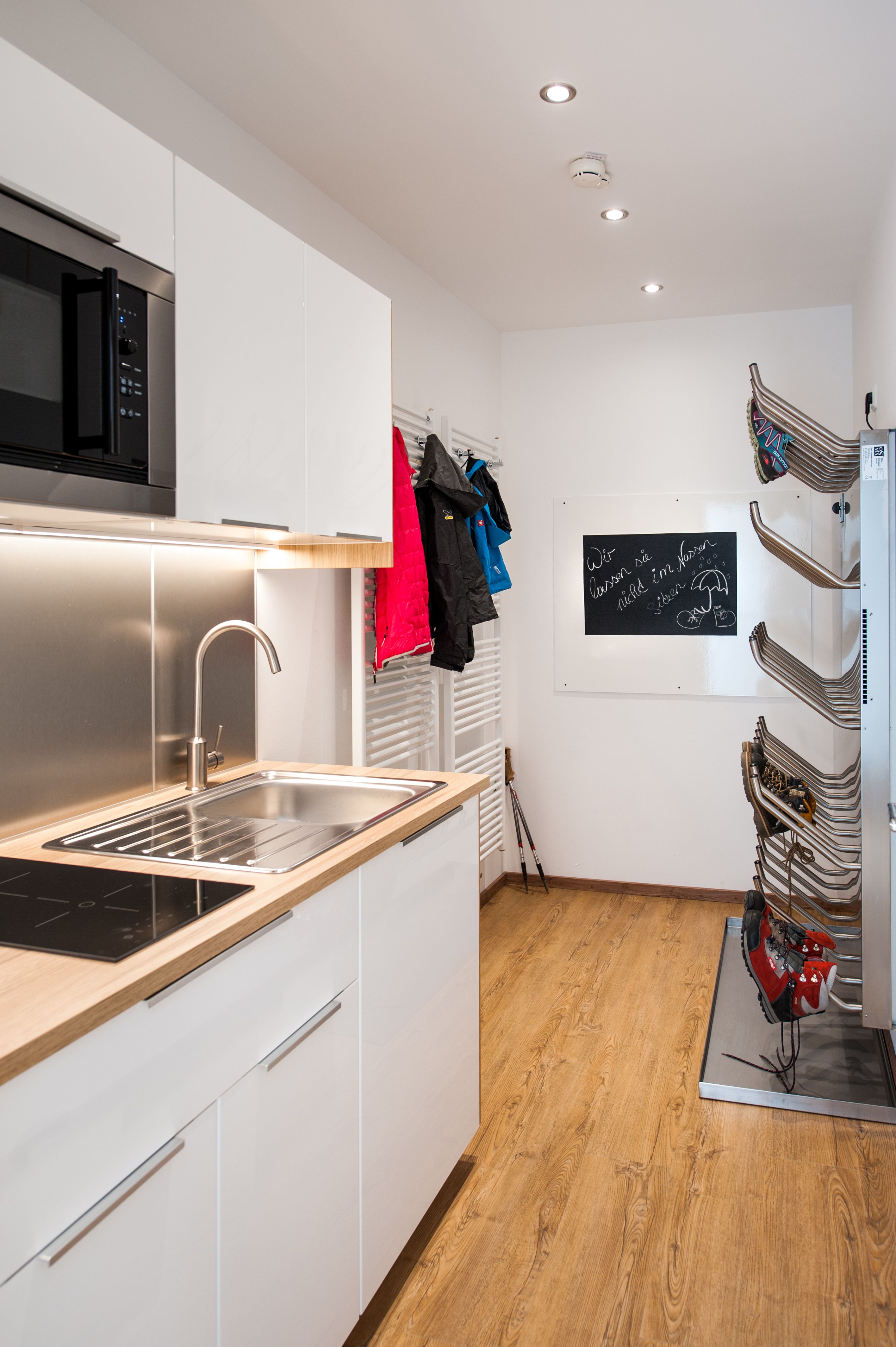 Modern kitchen with sink, microwave, jackets on hooks and ski boot dryer.