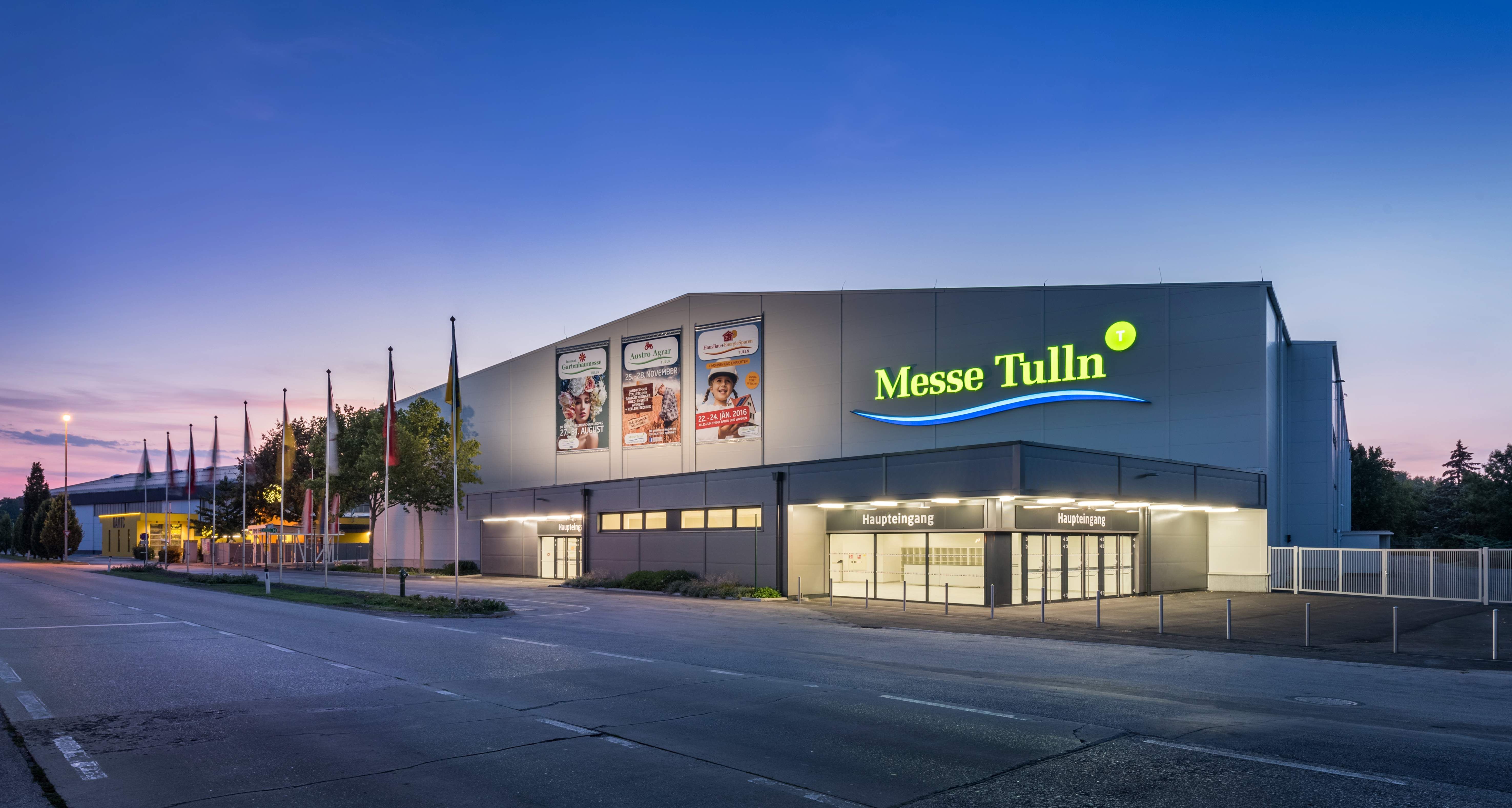 Exterior view of Messe Tulln at dusk with illuminated entrance and flags.