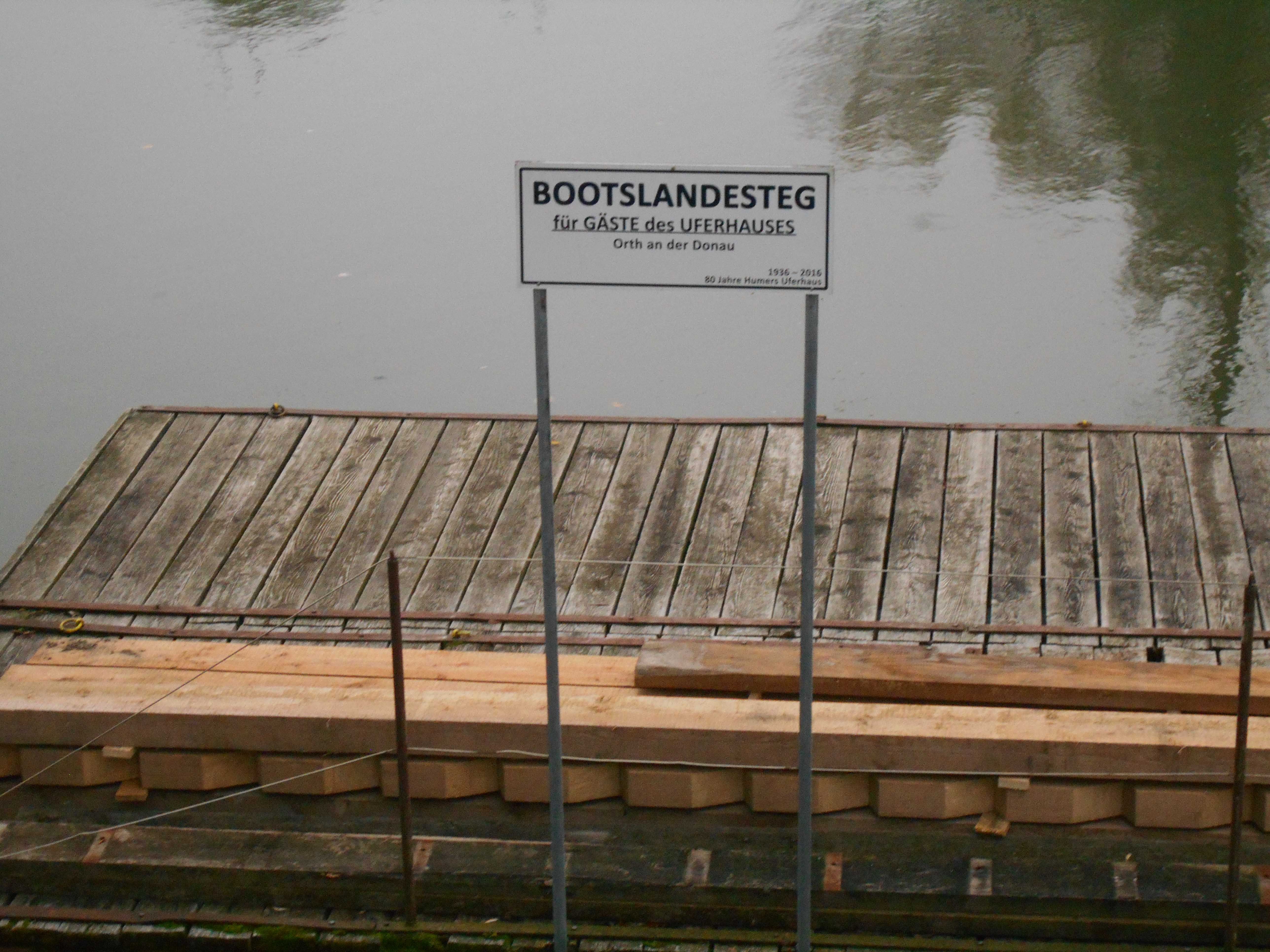 Wooden jetty with sign 'Boat landing stage for guests of the Uferhaus' on a quiet stretch of water.