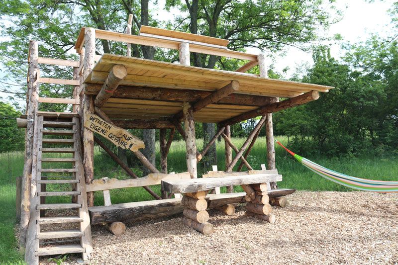 Wooden platform with table and hammock outdoors.