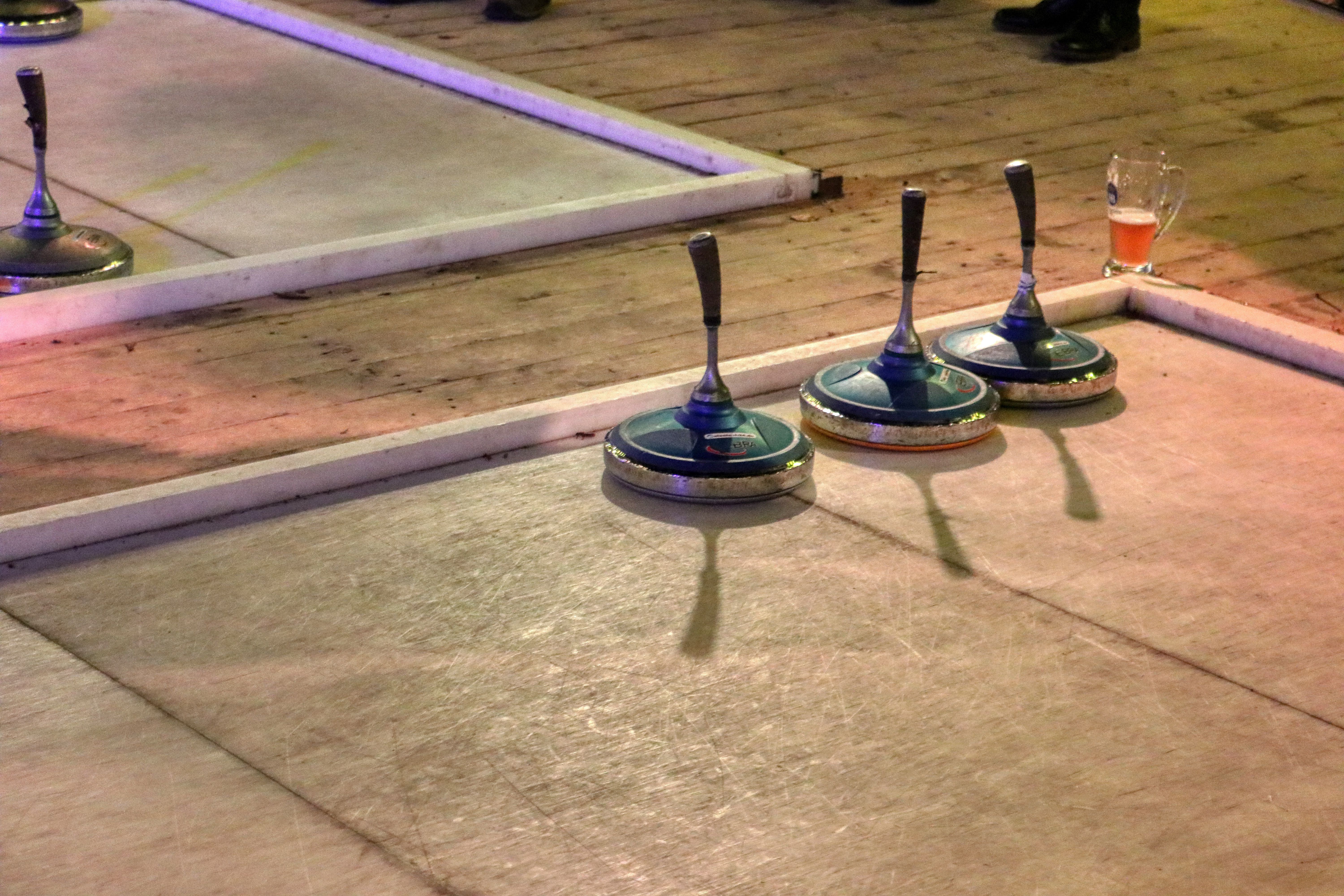 Three ice sticks stand on a curling rink, next to a glass with a drink.
