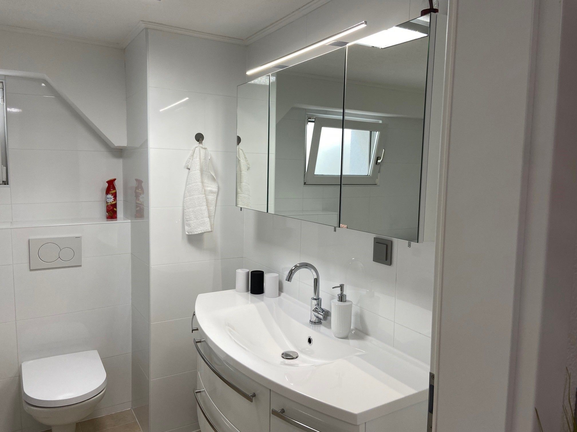 Modern bathroom with washbasin, mirror, toilet and small window.