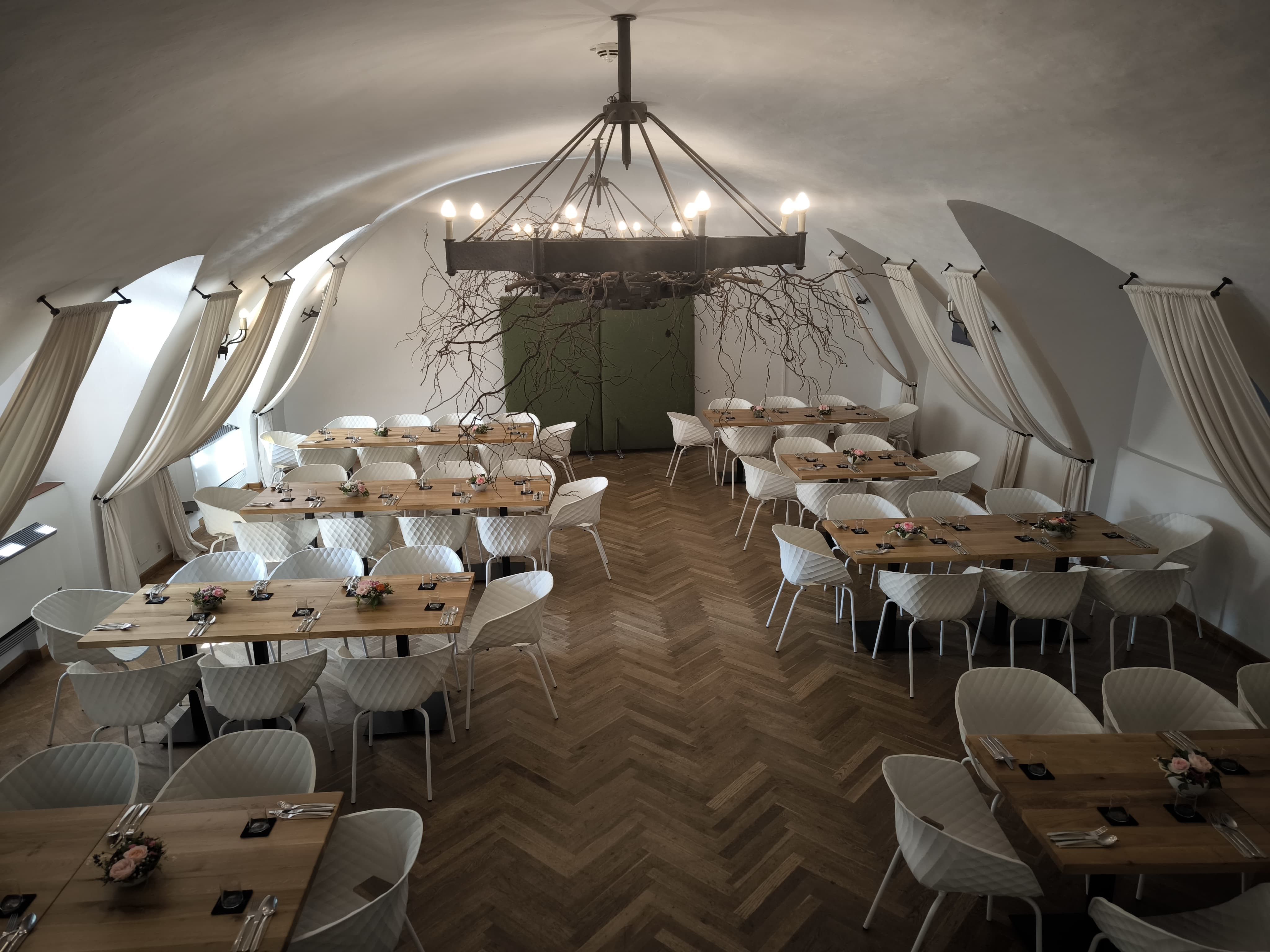 Elegant hall with wooden tables, parquet floor, white chairs and iron chandelier.