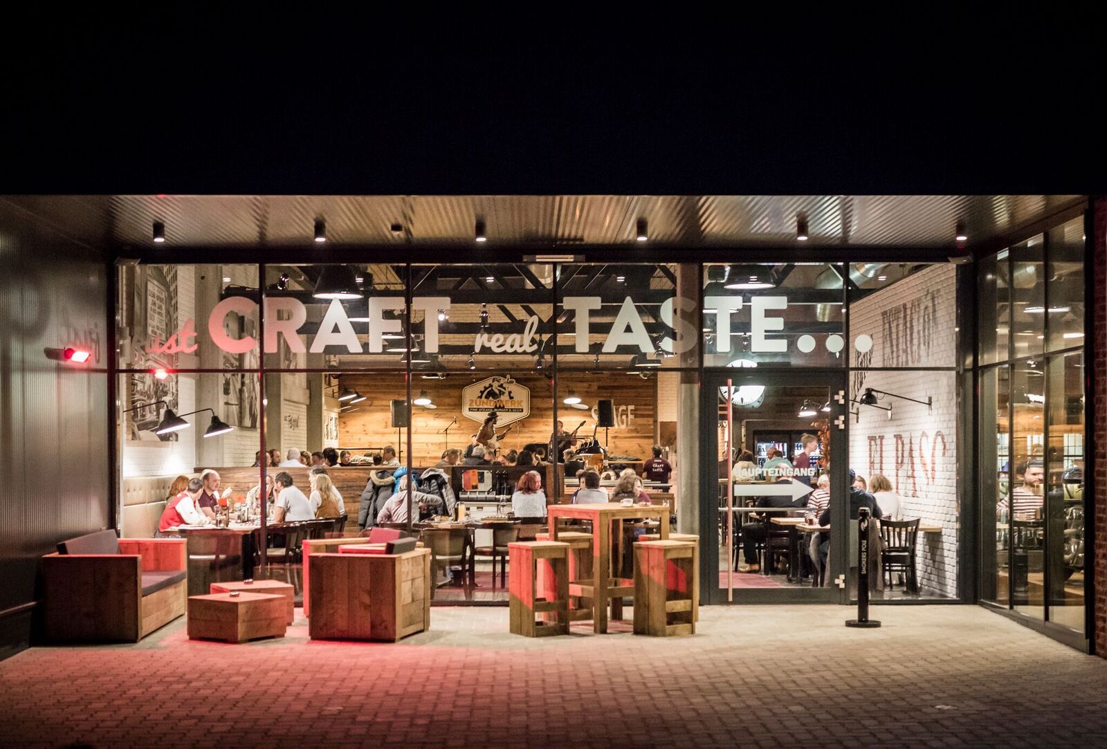 Exterior view of a restaurant with a glass front, inside people are sitting at tables.