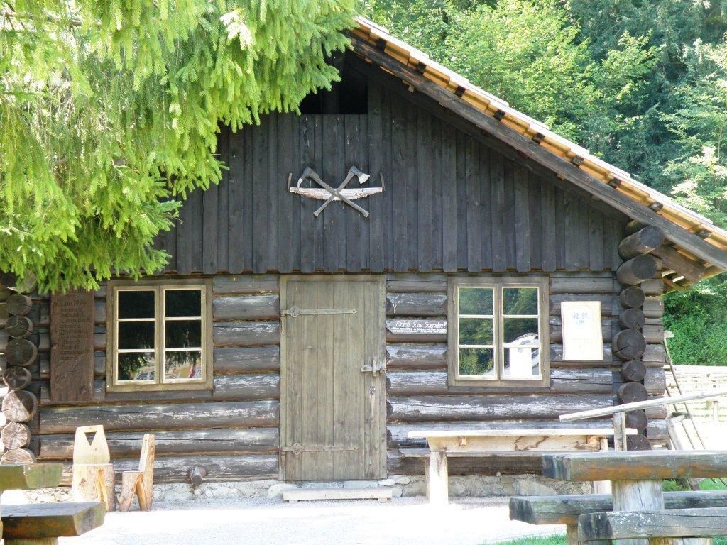 Wooden hut with two windows and a door, surrounded by trees.