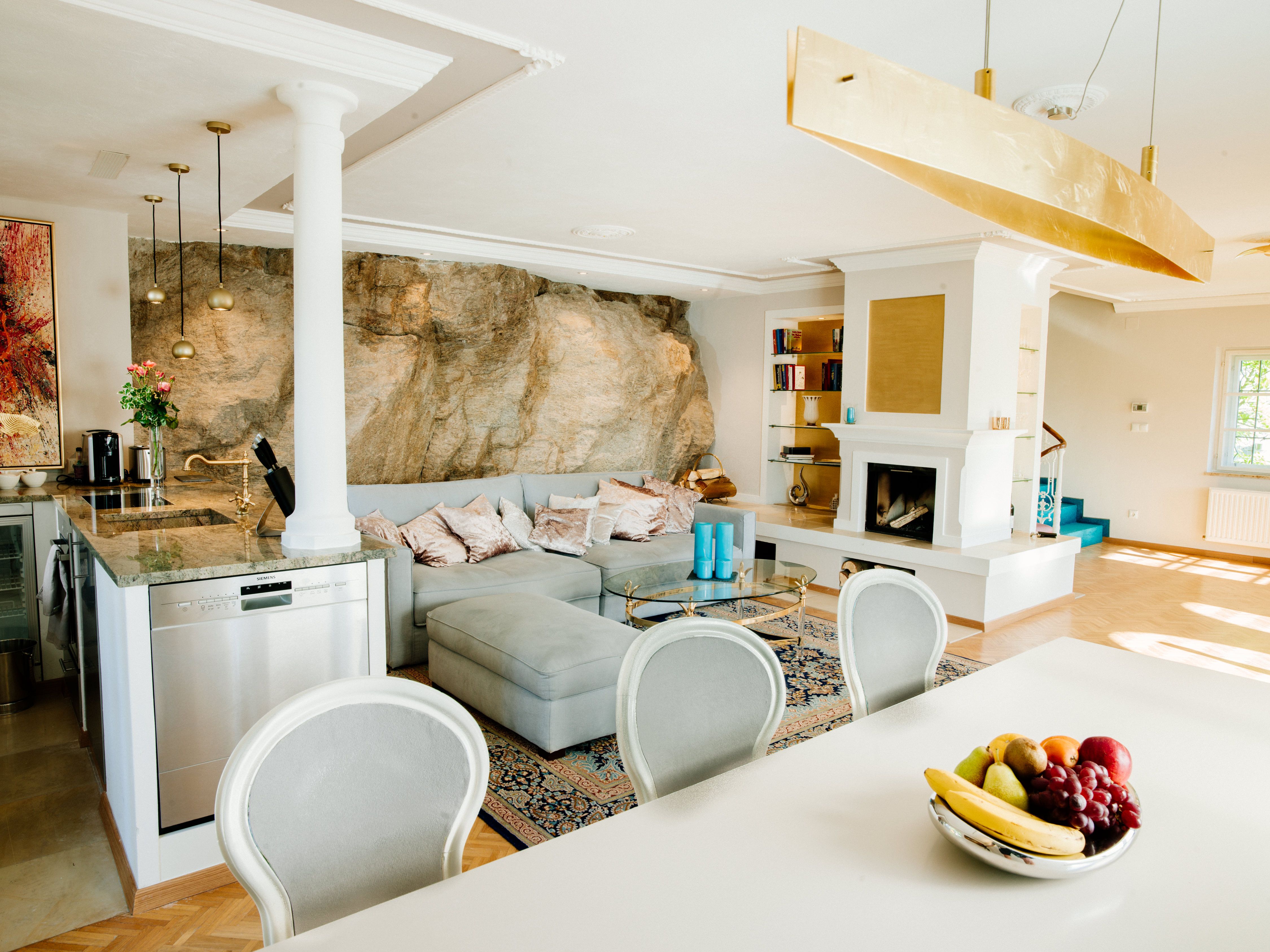 Elegant living room with modern kitchen, fireplace and rock wall.