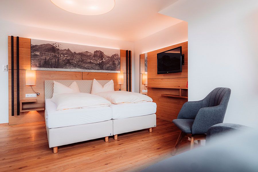 Modern hotel room with double bed, wooden floor and wall decoration.