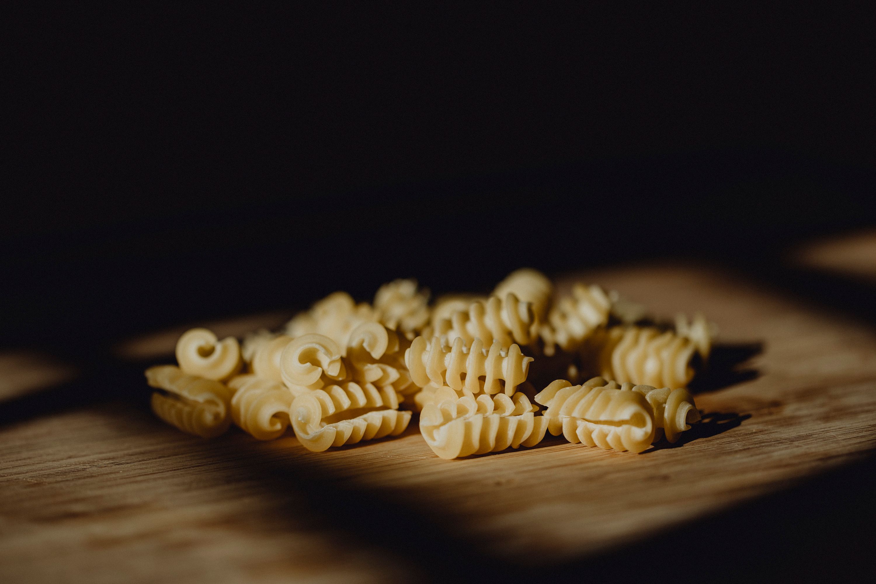 Close-up of uncooked, spiral-shaped noodles on a wooden base.
