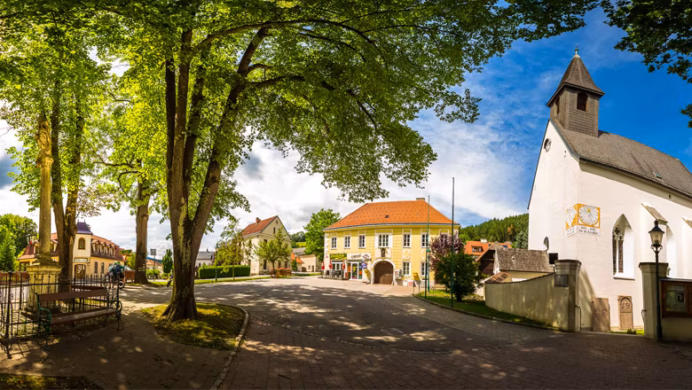 Panoramic view of the Feistritz church square with church, trees and historic buildings.