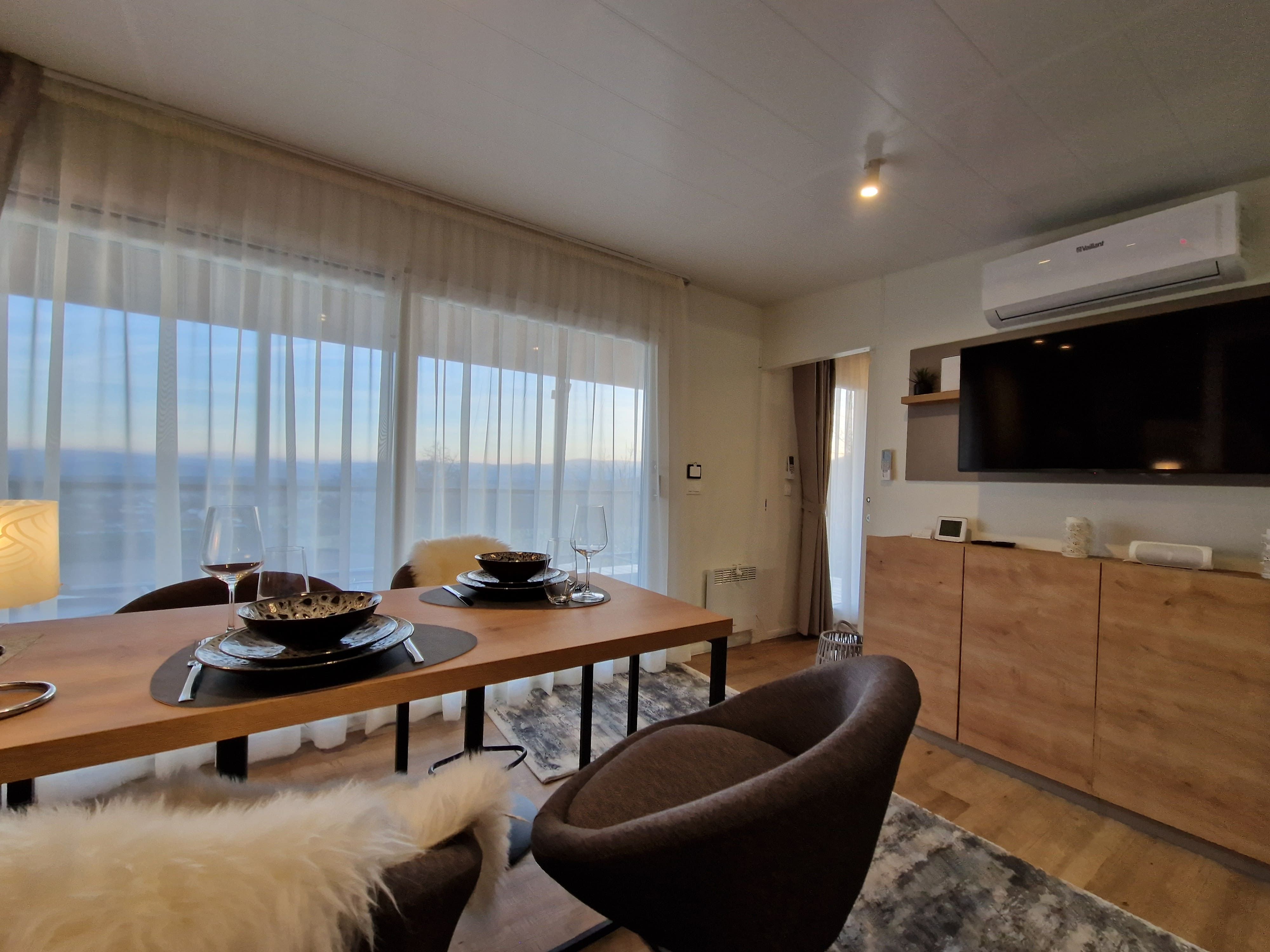 Modern living room with dining table, chairs, large window and TV.