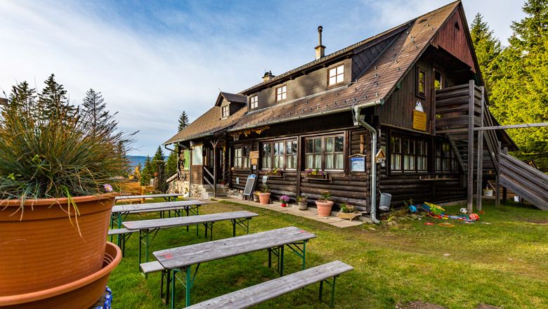 Wooden hut with outdoor beer benches, surrounded by trees.
