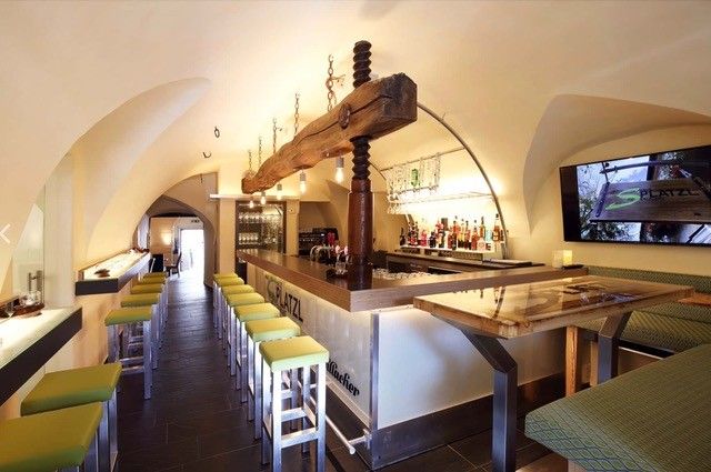 Interior view of a modern restaurant with bar, green stools and vaulted ceiling.