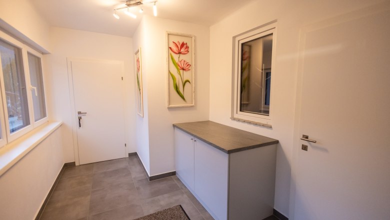 Modern entrance hall with gray tiled floor, white cabinet and flower picture on the wall.