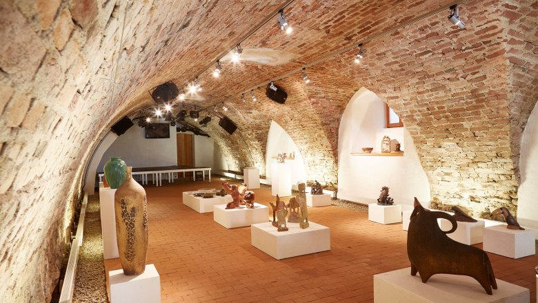 A vaulted cellar with works of art on plinths, illuminated by ceiling spotlights.