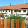 A white vacation home with a red tiled roof and wooden fence in the foreground.