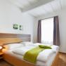 Bright bedroom with double bed, green bedspread and two small pictures on the wall.