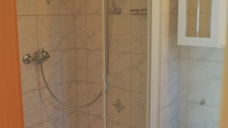 Small shower cubicle with tiles and shower head.