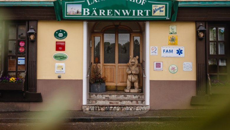 Entrance to the Landgasthof Bärenwirt with wooden figure of a bear and various signs on the wall.