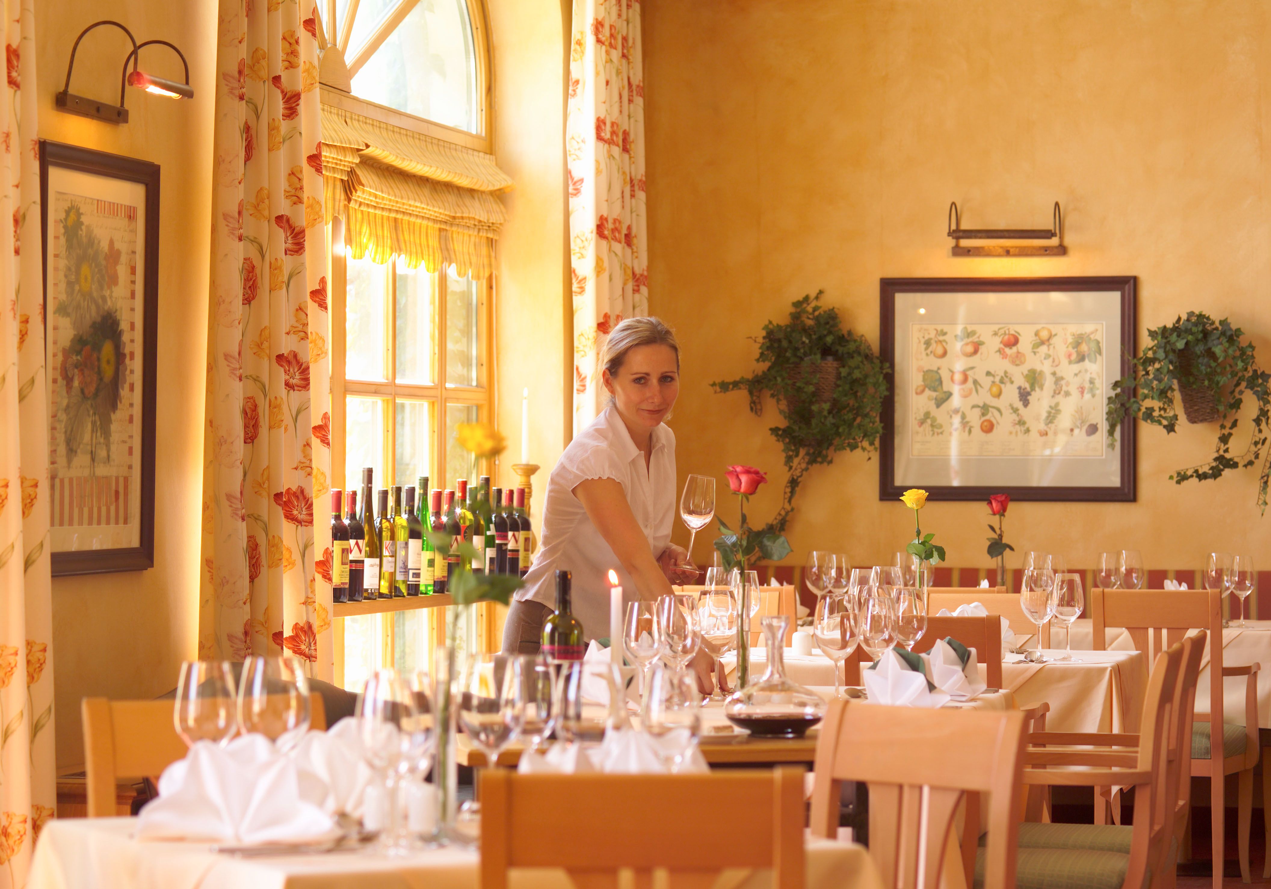 A woman sets tables in an elegant restaurant with wine glasses and flowers.