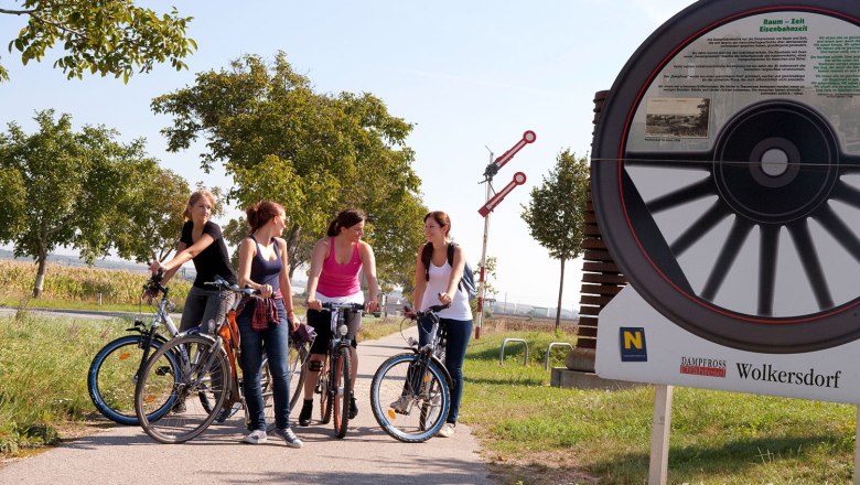 Four women with bicycles on a cycle path next to a large bicycle monument in Wolkersdorf.