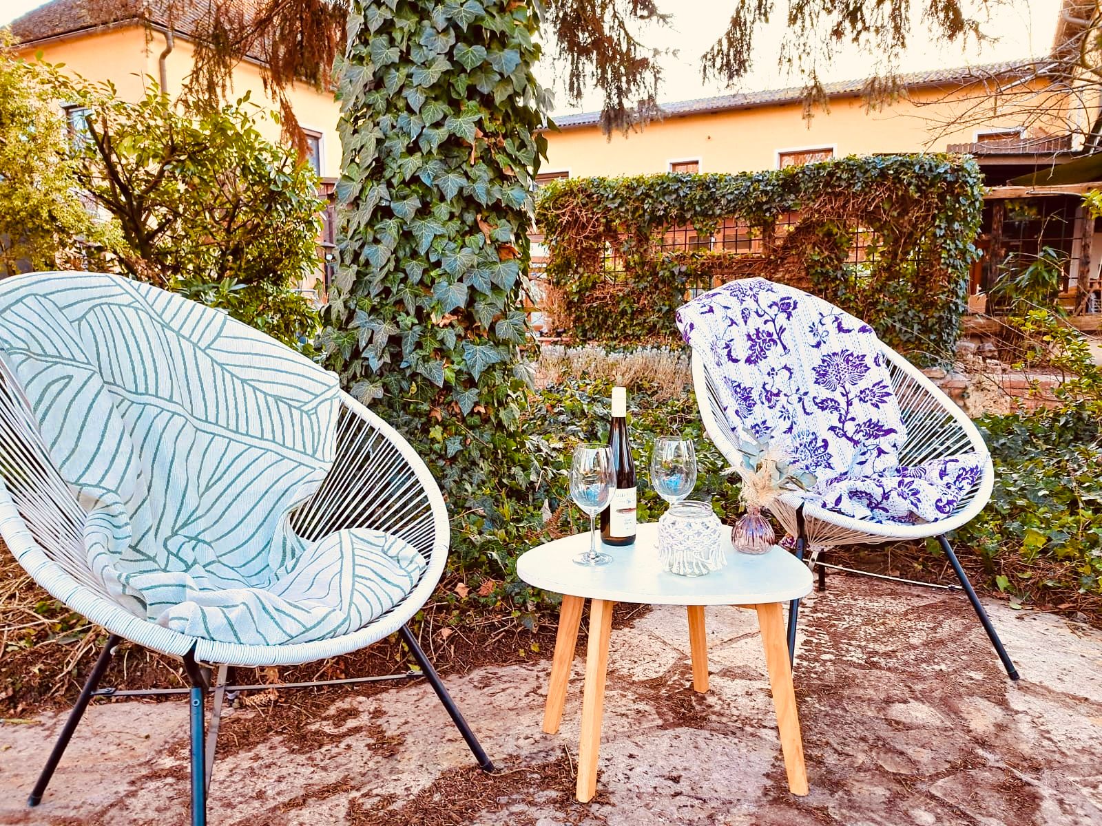 Two chairs with blankets and a table with wine and glasses in a garden.