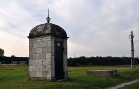 Stone building on a meadow with electricity pylon in the background.