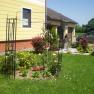 A well-tended garden with a flower bed and trellis in front of a yellow house.