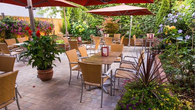 A cozy guest garden with tables, chairs and parasols, surrounded by lush plants.