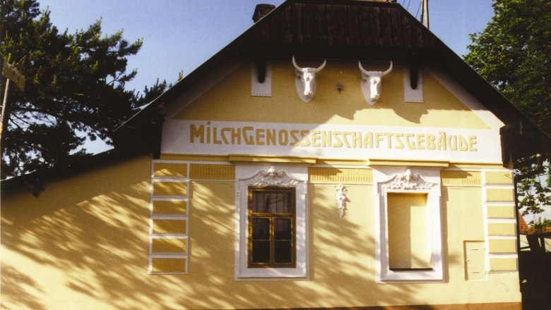 Yellow building with the inscription 'Milchgenossenschaftsgebäude' and two bulls' heads on the façade.