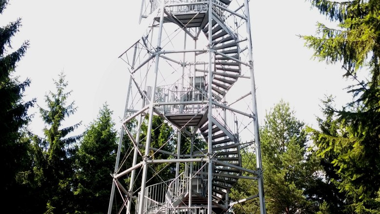 A tall metal observation tower with a spiral staircase in the forest.