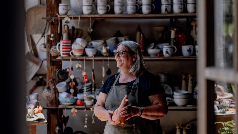 A woman in a pottery workshop, surrounded by ceramic dishes and decorations.