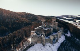 Aerial view of the ruins of Kirchschlag Castle in winter, surrounded by snow-covered forests.