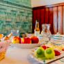 A table laid with fruit, bread and crockery in front of a green tiled wall.