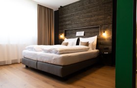 Modern hotel room with large bed, wooden wall and hanging lamps.