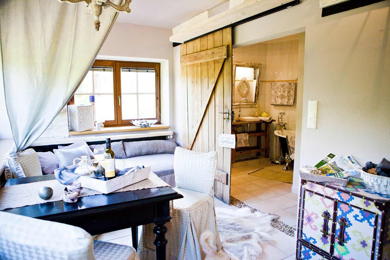 Cozy living room with wooden door, sofa, table and decorative elements, view into the bathroom.