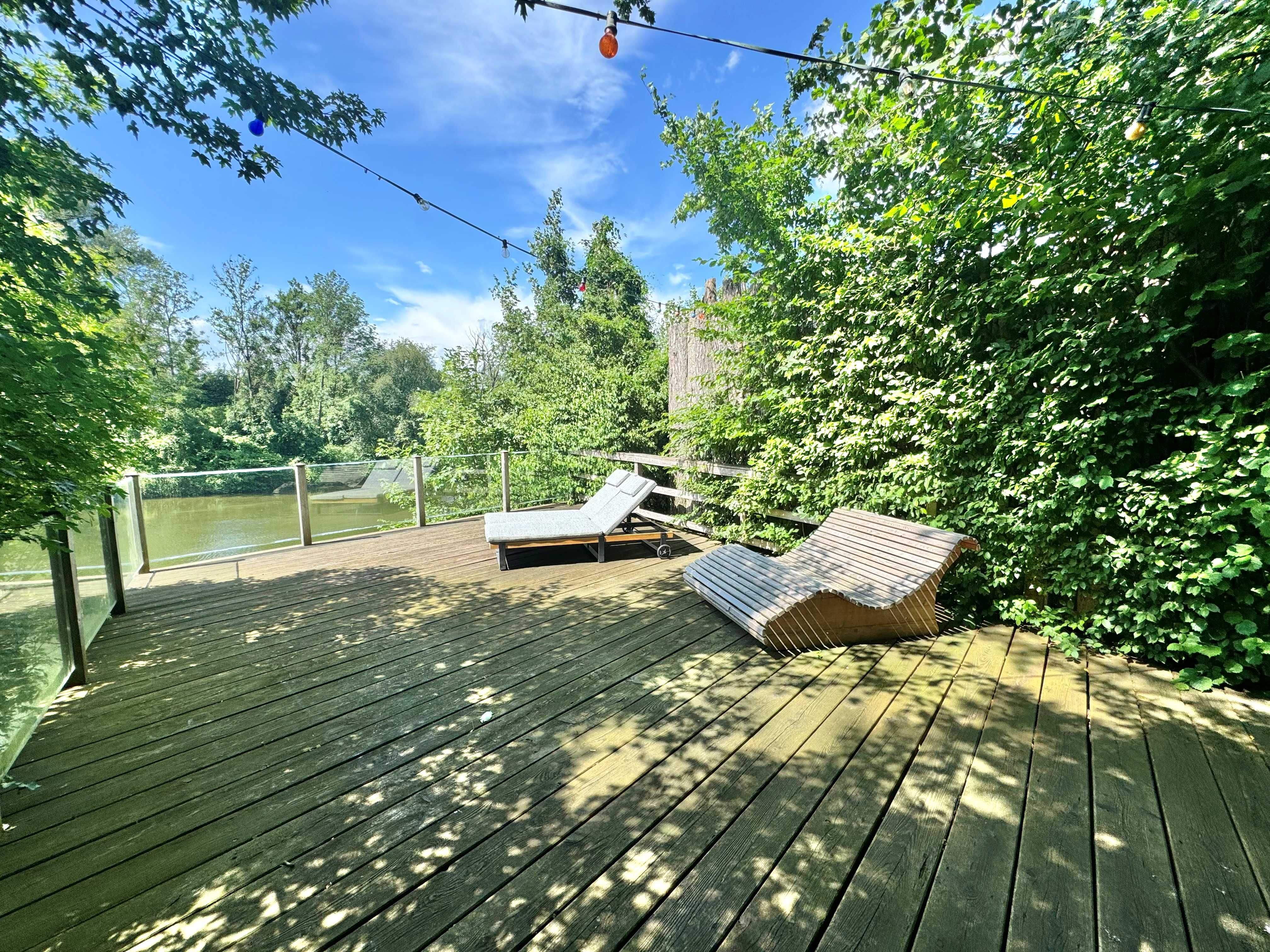 A wooden deck with lounge chairs and a view of the Ybbs River, surrounded by trees.