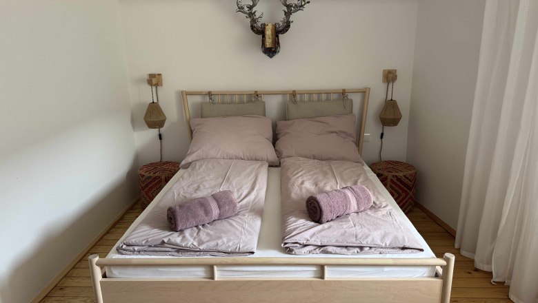 Bedroom with double bed, pink bed linen and towels, wooden floor and wall decoration.