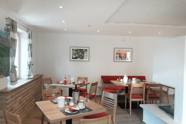 A cozy breakfast room with wooden tables, red upholstered benches and decorative pictures on the wall.