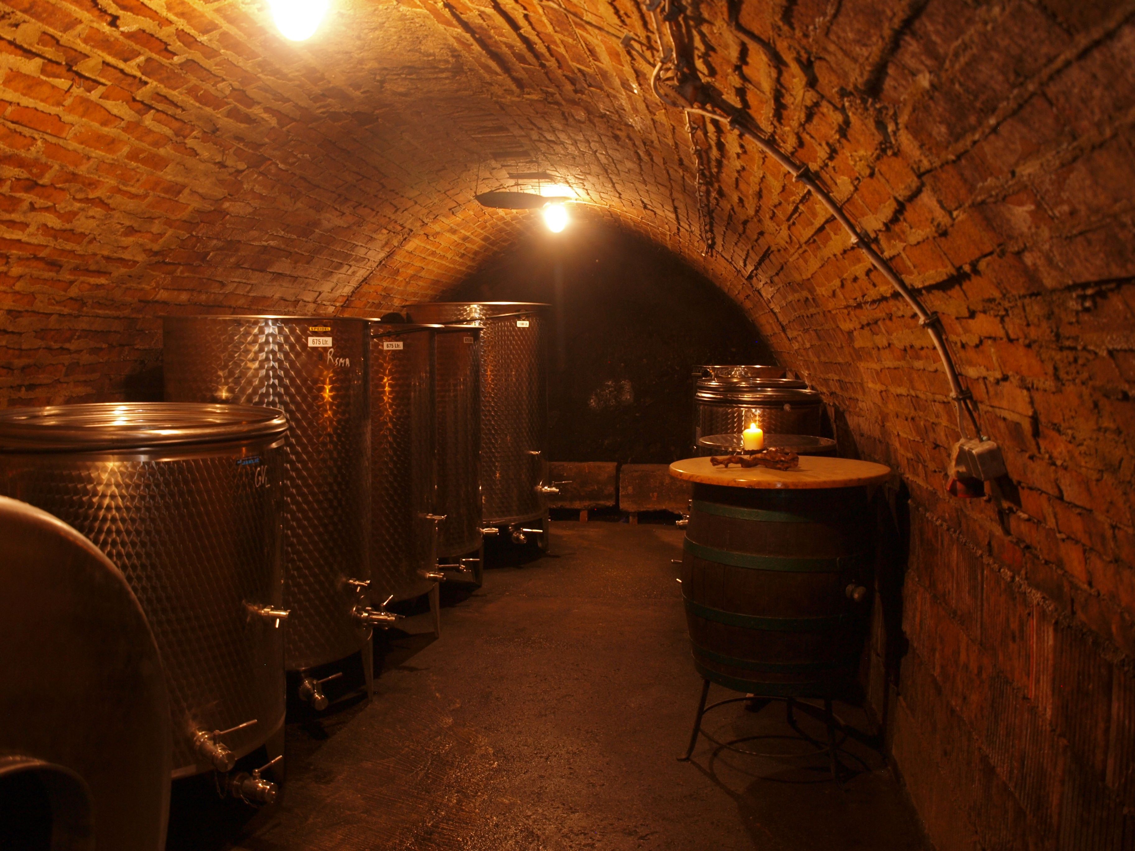 A wine cellar with metal tanks and a barrel, illuminated by warm light.