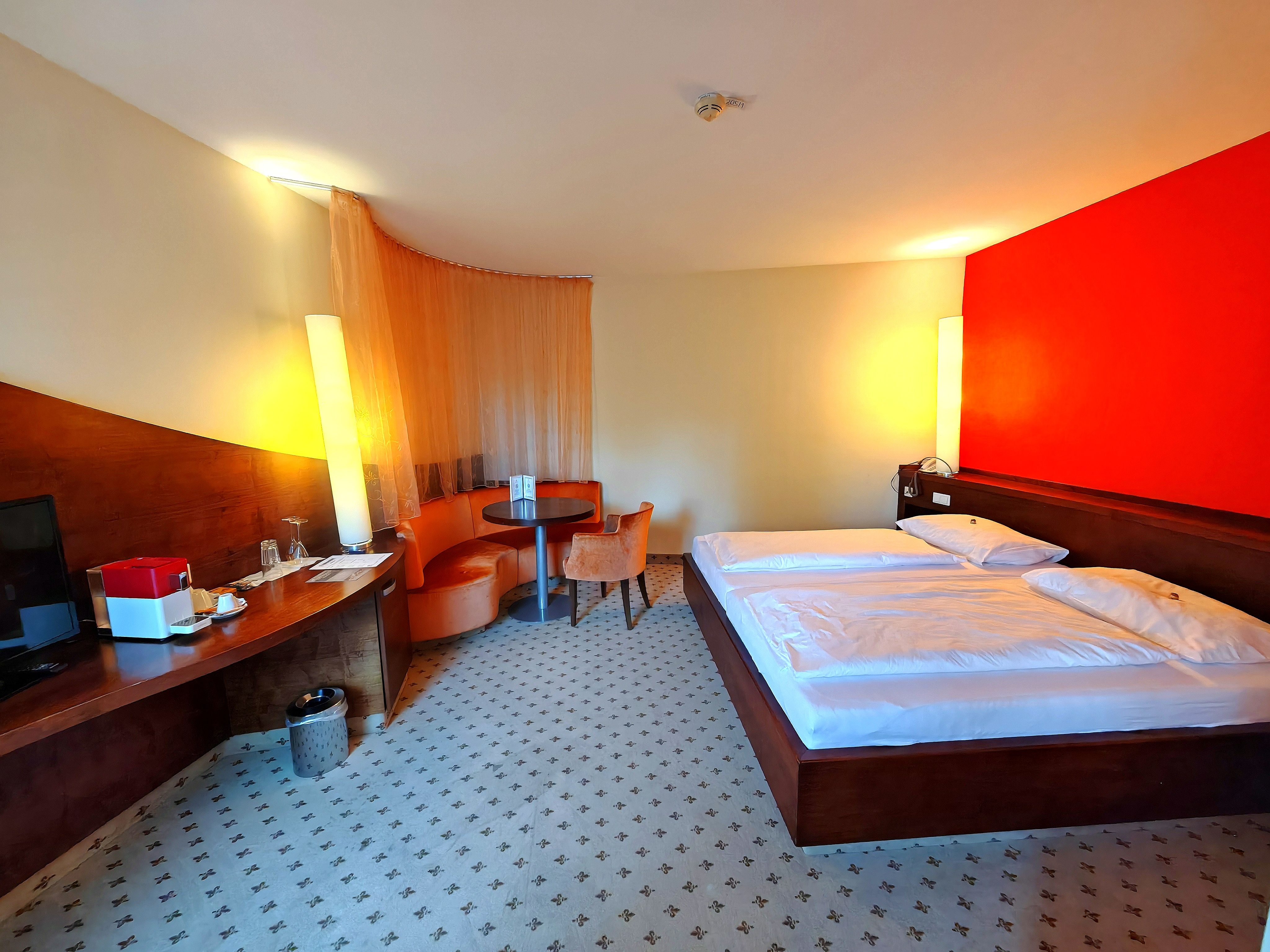 Hotel room with a double bed, a red accent wall, a desk, and a sitting area.